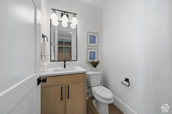 White single-panel interior door with matte black hardware opens to a bathroom featuring a light wood-finish vanity with a white countertop and integrated sink, matte black faucet, and a rectangular mirror