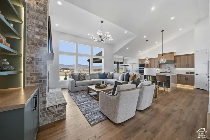 Great room featuring vaulted ceilings, wood-finish flooring, a brick fireplace with built-in shelving, an open-concept kitchen with pendant lighting, and expansive windows