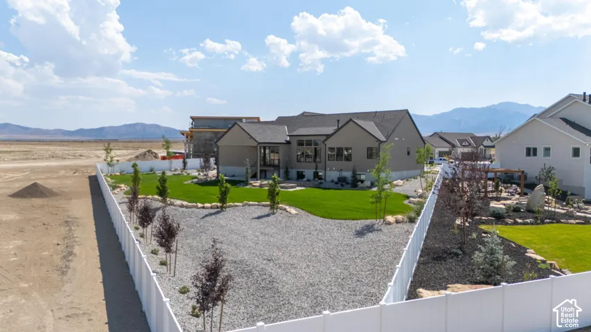 Contemporary residence featuring a neutral-toned exterior, a spacious backyard with manicured lawn, gravel landscaping, and a white privacy fence