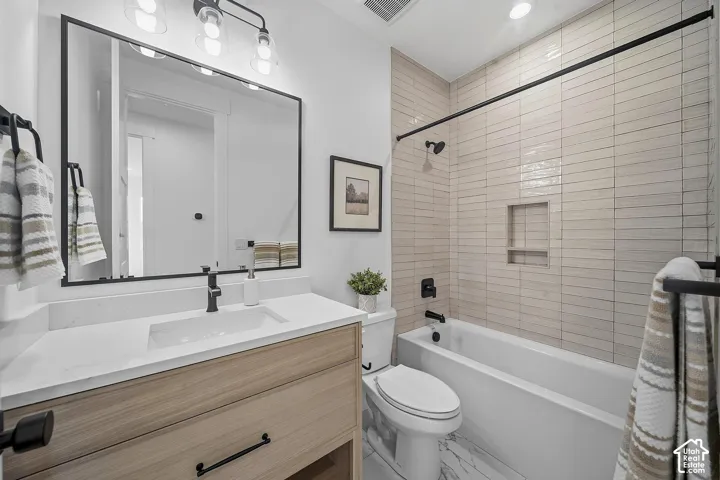 Bathroom featuring a light wood-finish vanity with a white countertop and integrated sink, a rectangular framed mirror, and a tub/shower combination with light horizontal tile surround and built-in niche