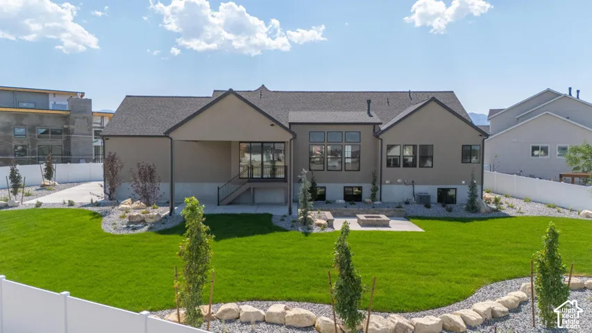 Expansive backyard featuring a manicured lawn, gravel landscaping with boulders, a built-in fire pit, and a covered patio area