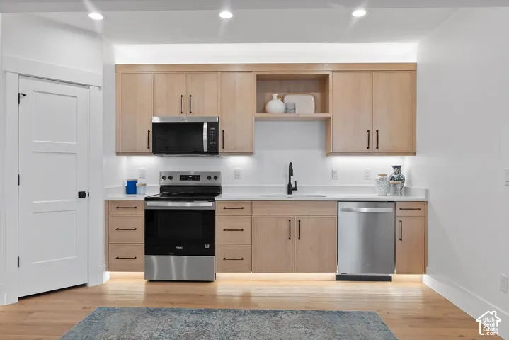 Modern kitchen featuring natural wood-finish cabinetry with stainless steel hardware, white subway tile backsplash, and a full suite of stainless steel appliances including a gas range, microwave, and dishwasher
