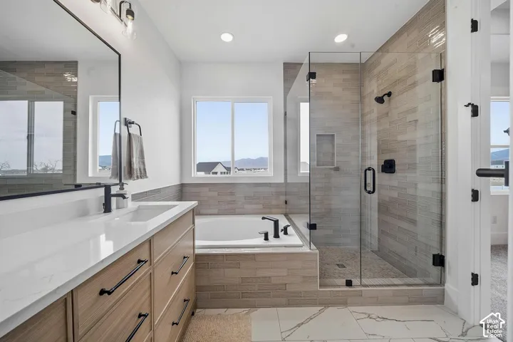 Modern bathroom featuring a glass-enclosed shower with subway tile surround, a built-in soaking tub, and a vanity with a white countertop and natural wood-finish cabinetry