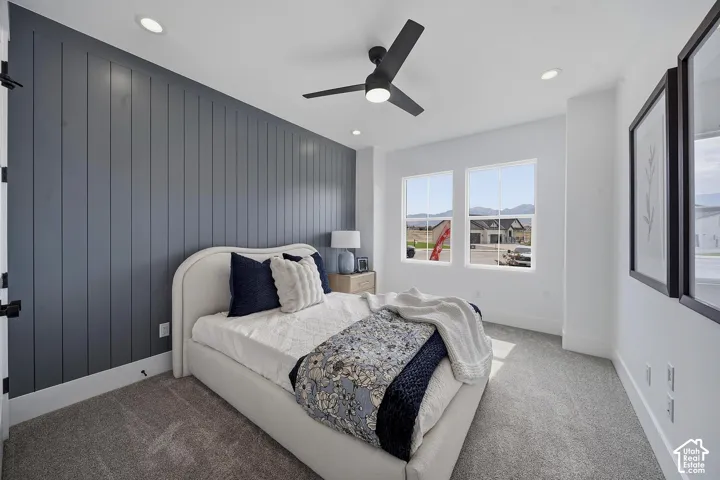 Modern primary bedroom featuring a curved upholstered bed frame, dark vertical shiplap accent wall, ceiling fan with integrated lighting, carpet flooring, and dual windows with natural light exposure