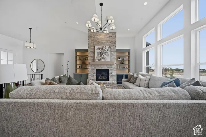 Vaulted great room with a stone fireplace, built-in shelving, expansive windows, and a black chandelier