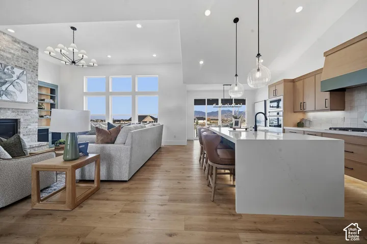 Open-concept living and kitchen area featuring hardwood flooring throughout, a large island with waterfall-edge countertop and seating for multiple guests, stainless steel appliances including a gas cooktop, white cabinetry with warm wood accents, pendant