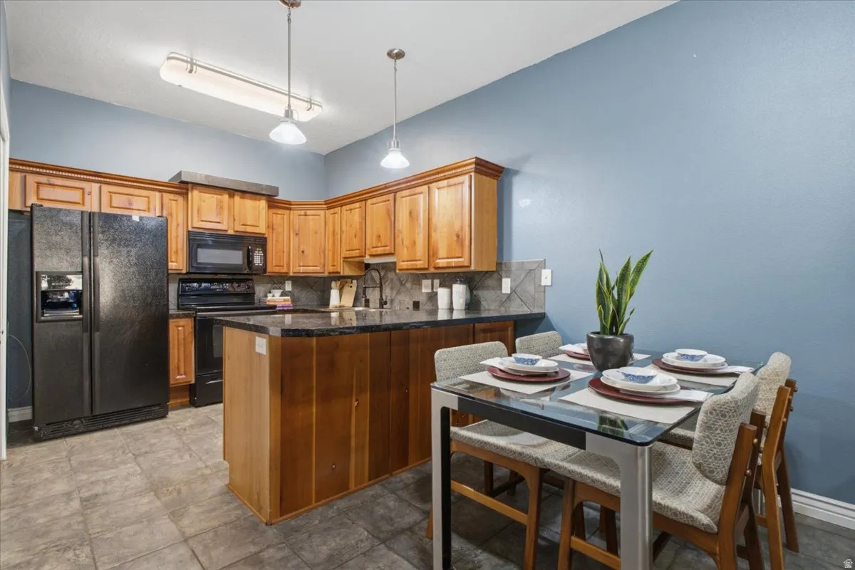 Kitchen featuring wood cabinetry, black appliances, dark countertops, and tile flooring