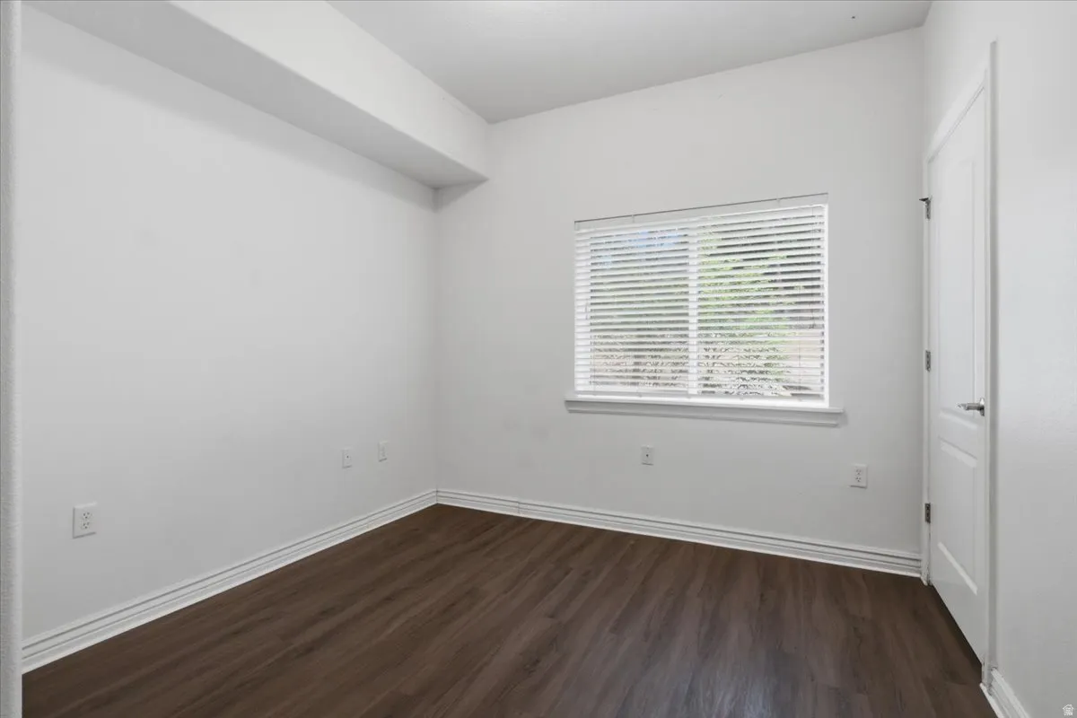 Room featuring wood-finish flooring, white baseboards, and a window with horizontal blinds