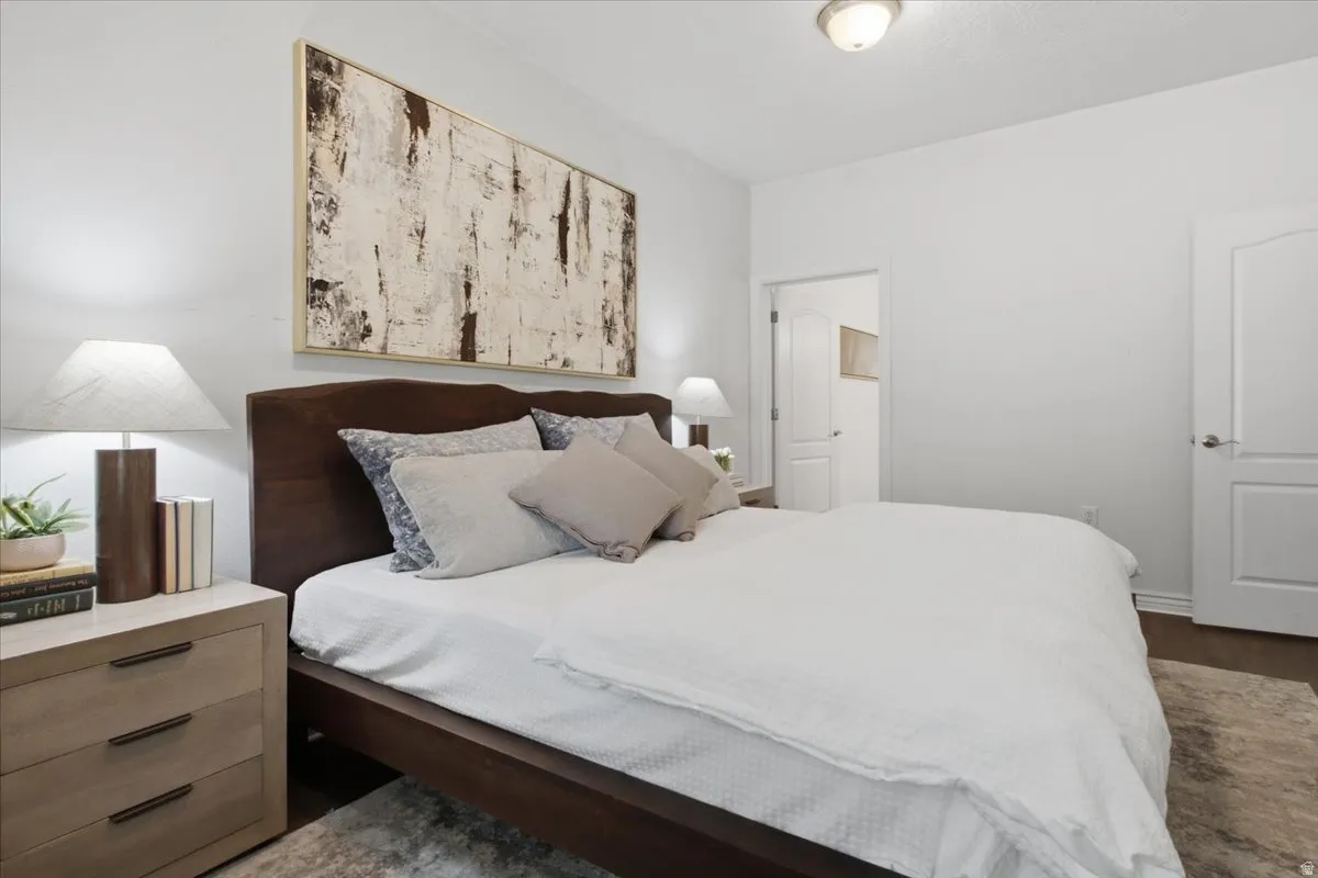 Spacious bedroom featuring dark wood-finish flooring, light neutral walls, and a modern ceiling light fixture