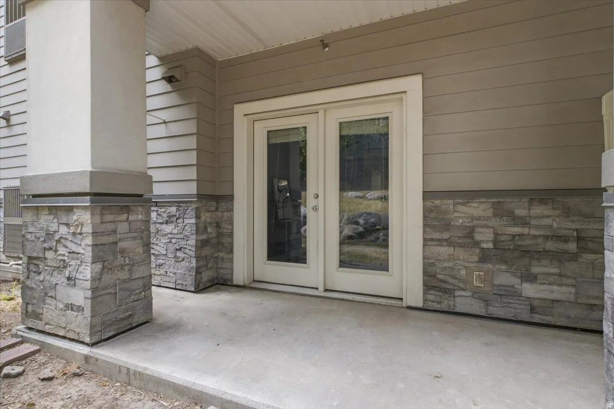 Outdoor patio with double French doors, concrete flooring, stone-clad pillars, and horizontal siding