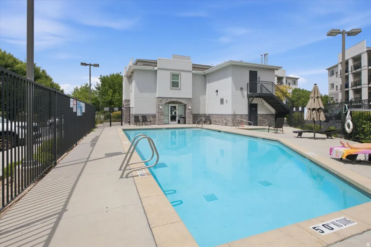 Rectangular swimming pool with integrated steps, surrounded by a concrete deck and a black metal fence