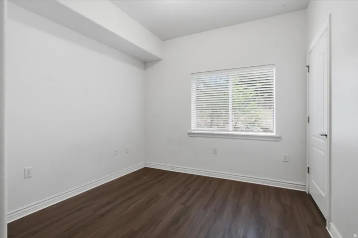 Room featuring wood-finish flooring, white baseboards, and a window with horizontal blinds