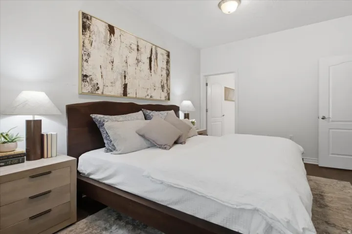 Spacious bedroom featuring dark wood-finish flooring, light neutral walls, and a modern ceiling light fixture