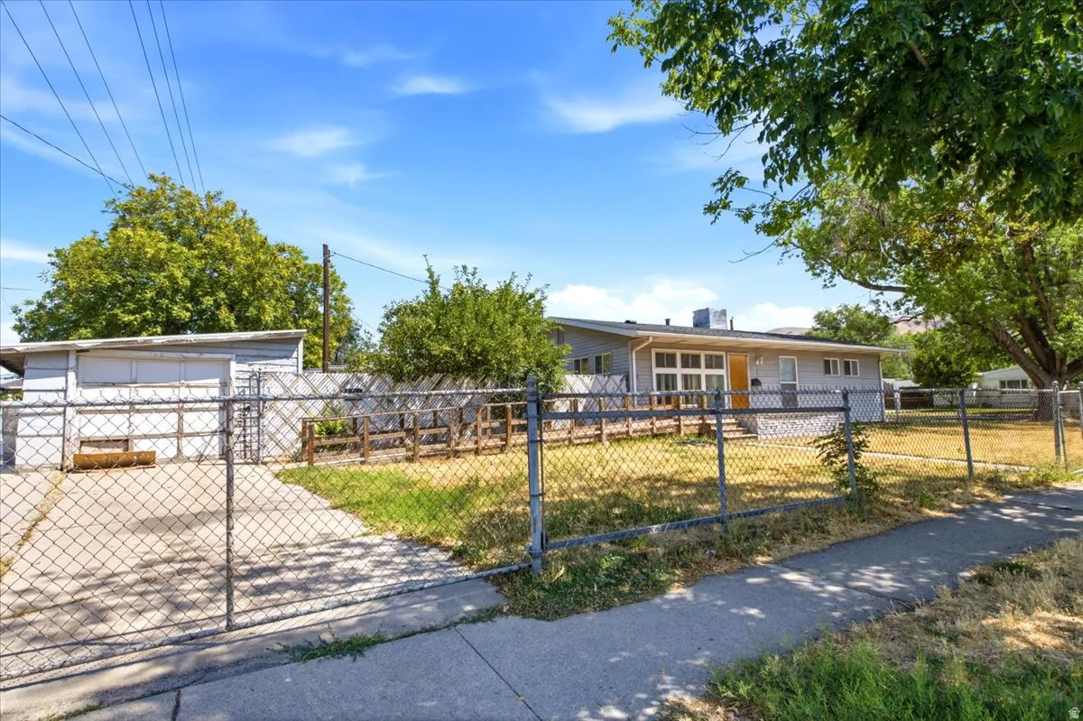 Fenced property featuring a concrete driveway, a separate storage building, and a main residence with a sloped roofline and exterior wood deck