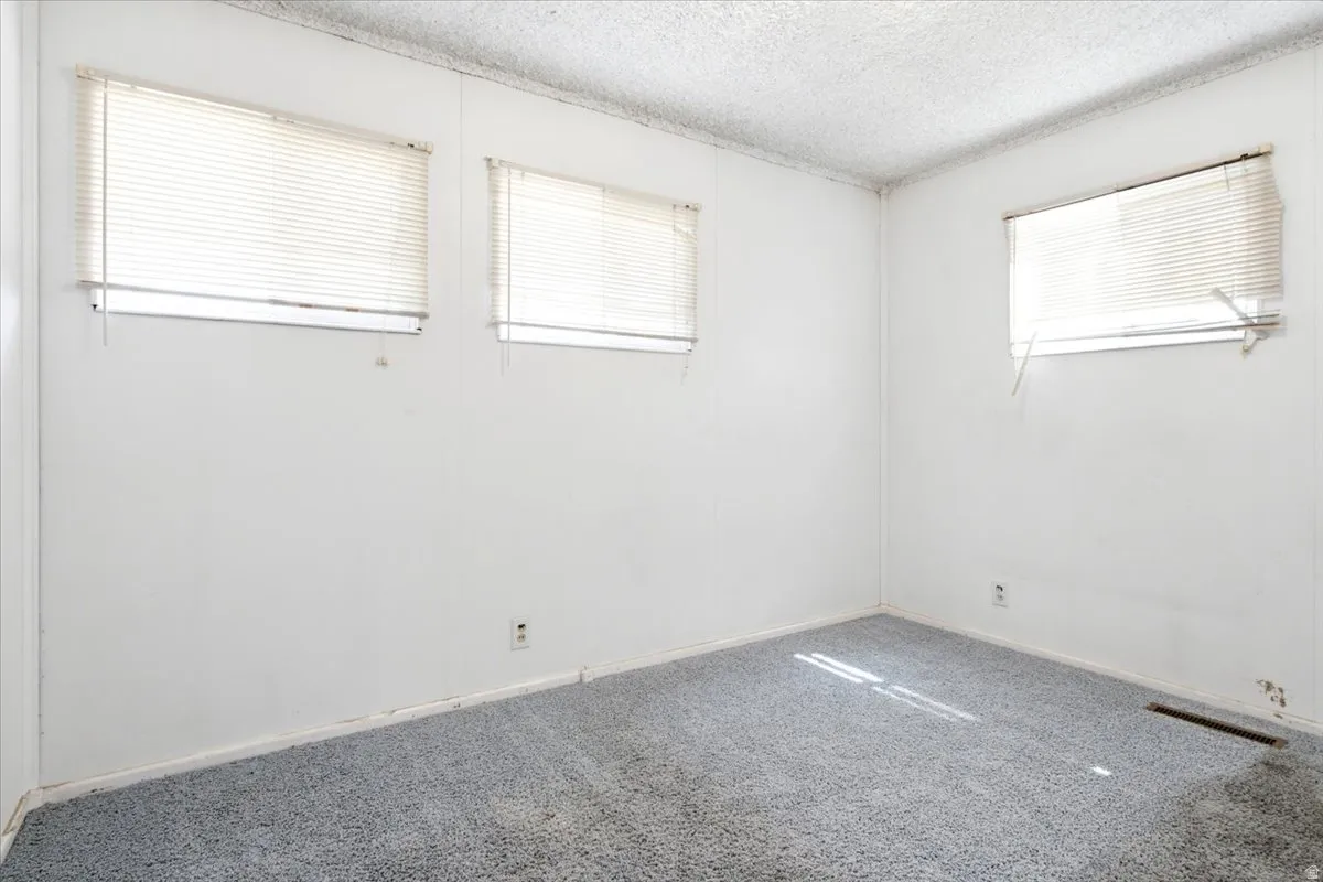 Room featuring light gray carpet, white walls, and three windows with horizontal blinds