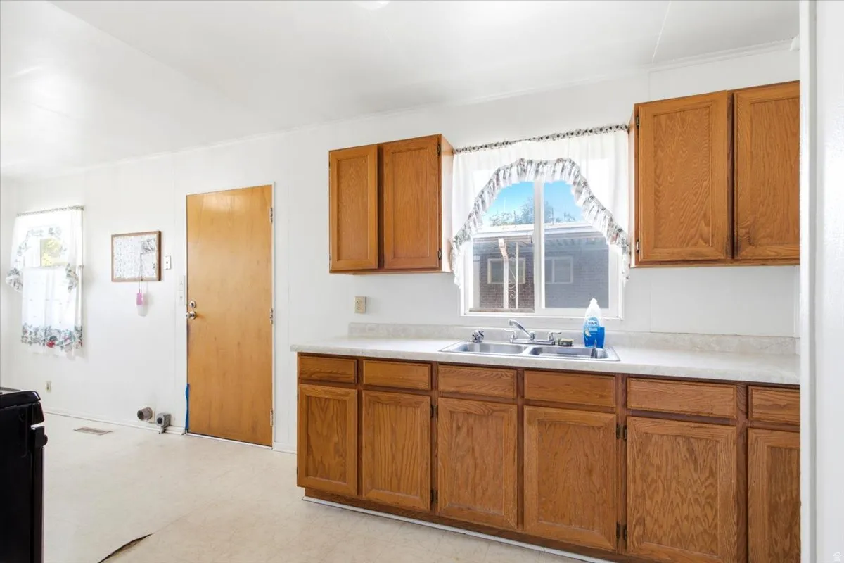 Kitchen area featuring wood-finish cabinetry, a double basin stainless steel sink, and light-toned countertops