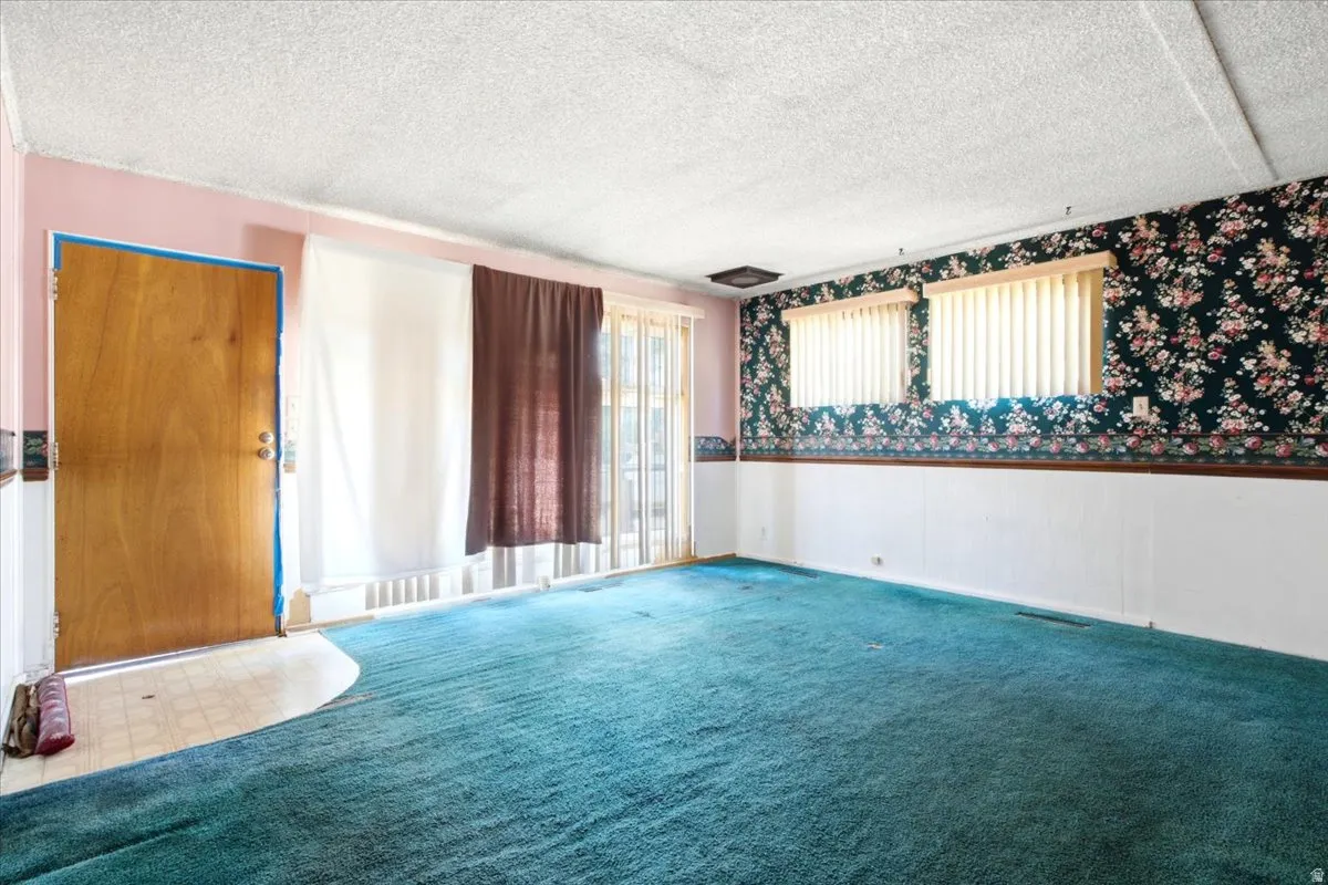 Spacious room featuring teal carpeting, paneled walls, and floral wallpaper accents
