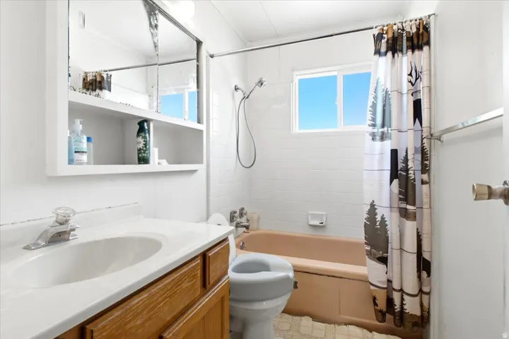 Bathroom featuring a single vanity with wood-finish cabinetry, a ceramic sink, and a mirrored medicine cabinet with open shelving