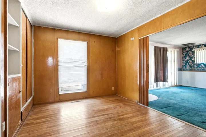 Room featuring wood-finish flooring, built-in shelving, and a single window with blinds