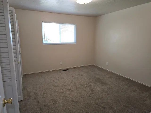 Neutral-toned room with plush carpeting, featuring a window with blinds, baseboard molding, and louvered bi-fold closet doors