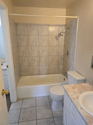 Full bathroom featuring a tiled shower-over-tub combination, ceramic floor tiling, and a vanity with an integrated sink and countertop