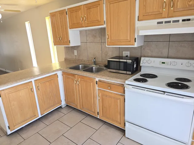 Kitchen featuring light wood cabinetry, stone-look countertops, and a tile backsplash