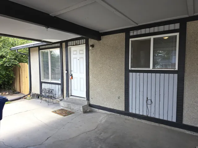 Covered entryway featuring a white paneled door, concrete steps, and stucco siding