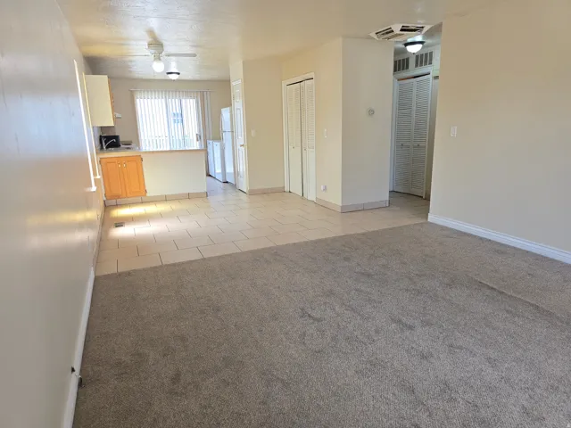 Open-concept living space featuring neutral-toned carpeting, light-colored tile flooring, and a kitchen area with wood-finish cabinetry