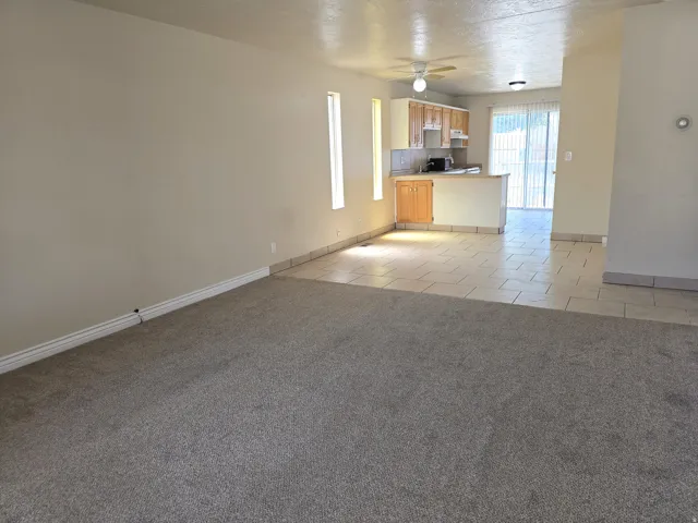Open concept living area featuring carpeted flooring and a kitchen with wood-finish cabinetry, tile flooring, and a breakfast bar