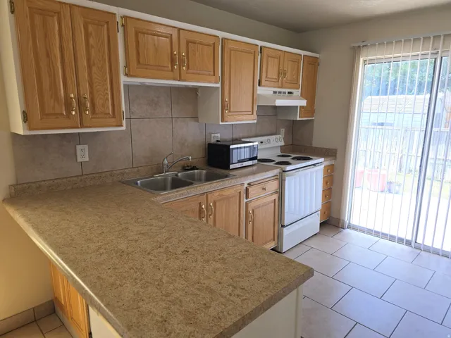 Kitchen featuring wood-finish cabinetry, speckled countertops, dual basin sink, and tile flooring