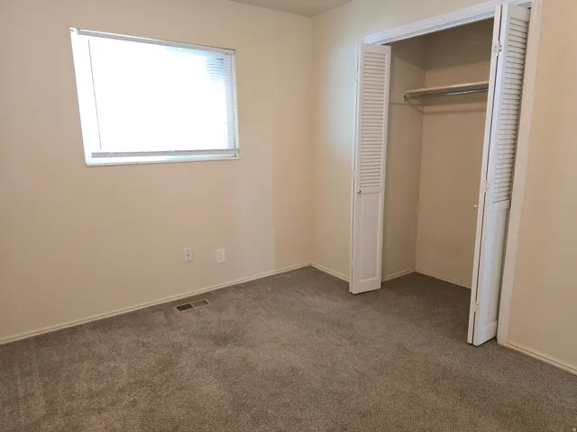 Carpeted room featuring a single window with blinds and a bi-fold louvered closet with a hanging rod and shelf