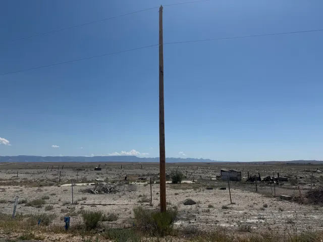 Expansive vacant land featuring a clear blue sky, distant mountain ranges, and scattered desert vegetation