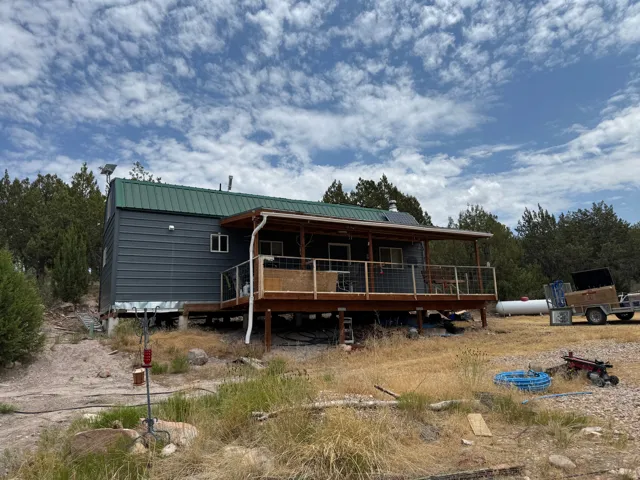 Gray metal siding exterior with a green metal roof and a spacious wood-deck porch featuring a metal railing
