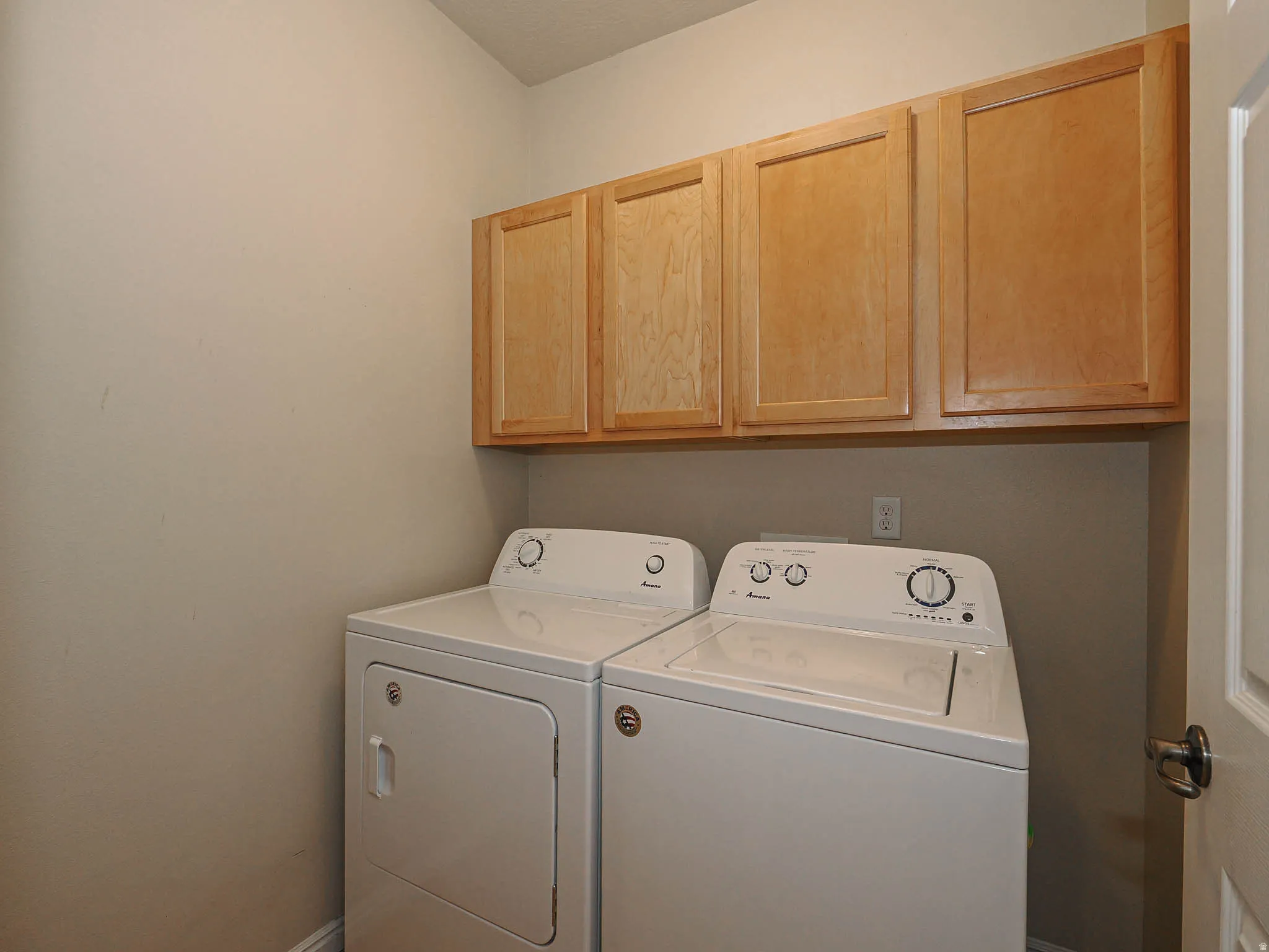 Laundry area featuring light wood-finish cabinetry, neutral wall tones, and overhead storage