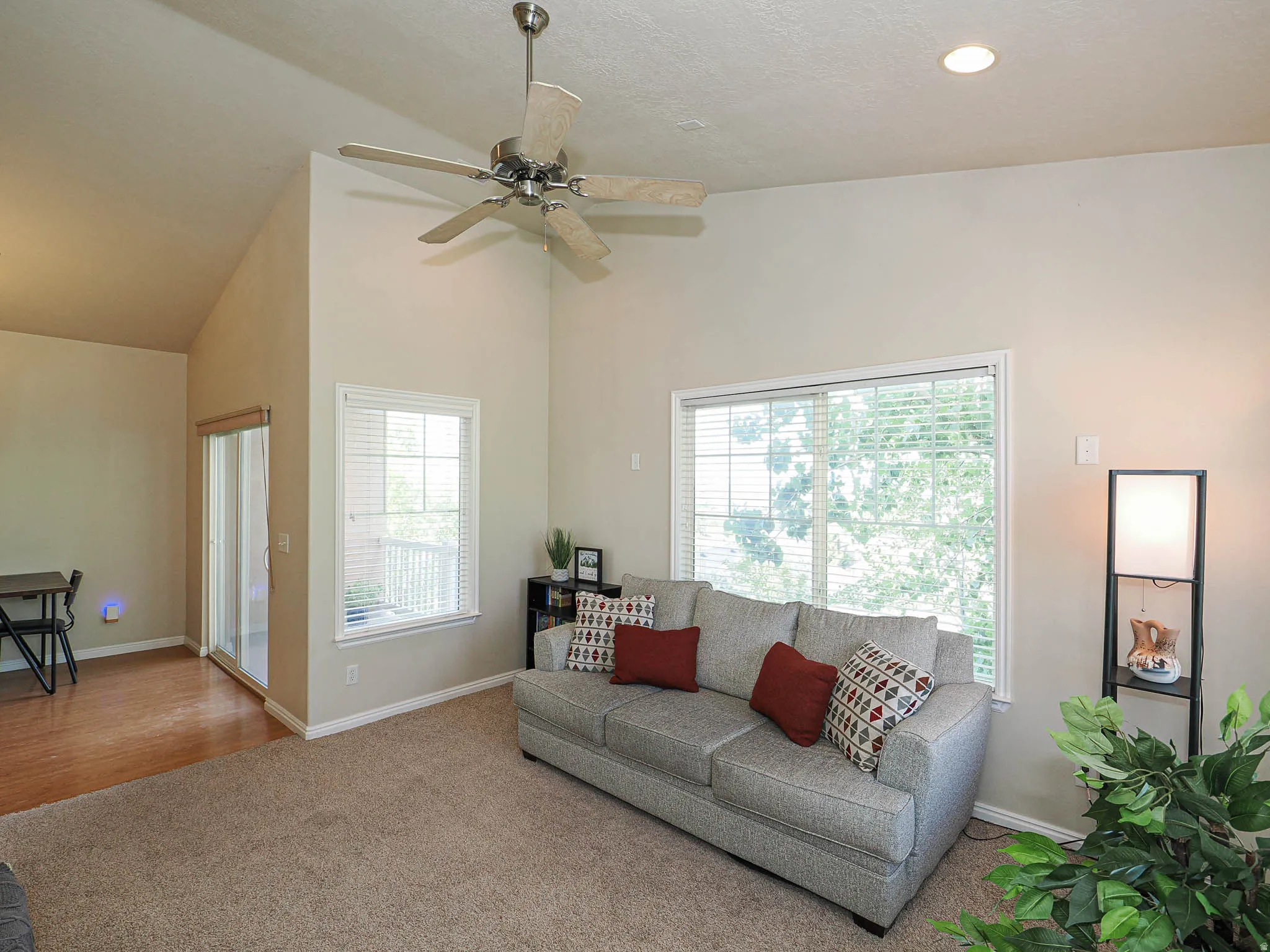 Living area featuring vaulted ceilings, recessed lighting, a ceiling fan, a large window with blinds, and a sliding glass door