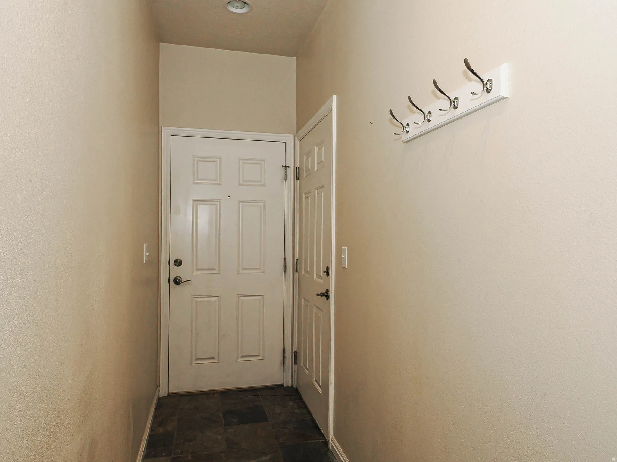 Entryway featuring durable dark tile flooring, a recessed ceiling light, and a white coat rack with chrome hooks