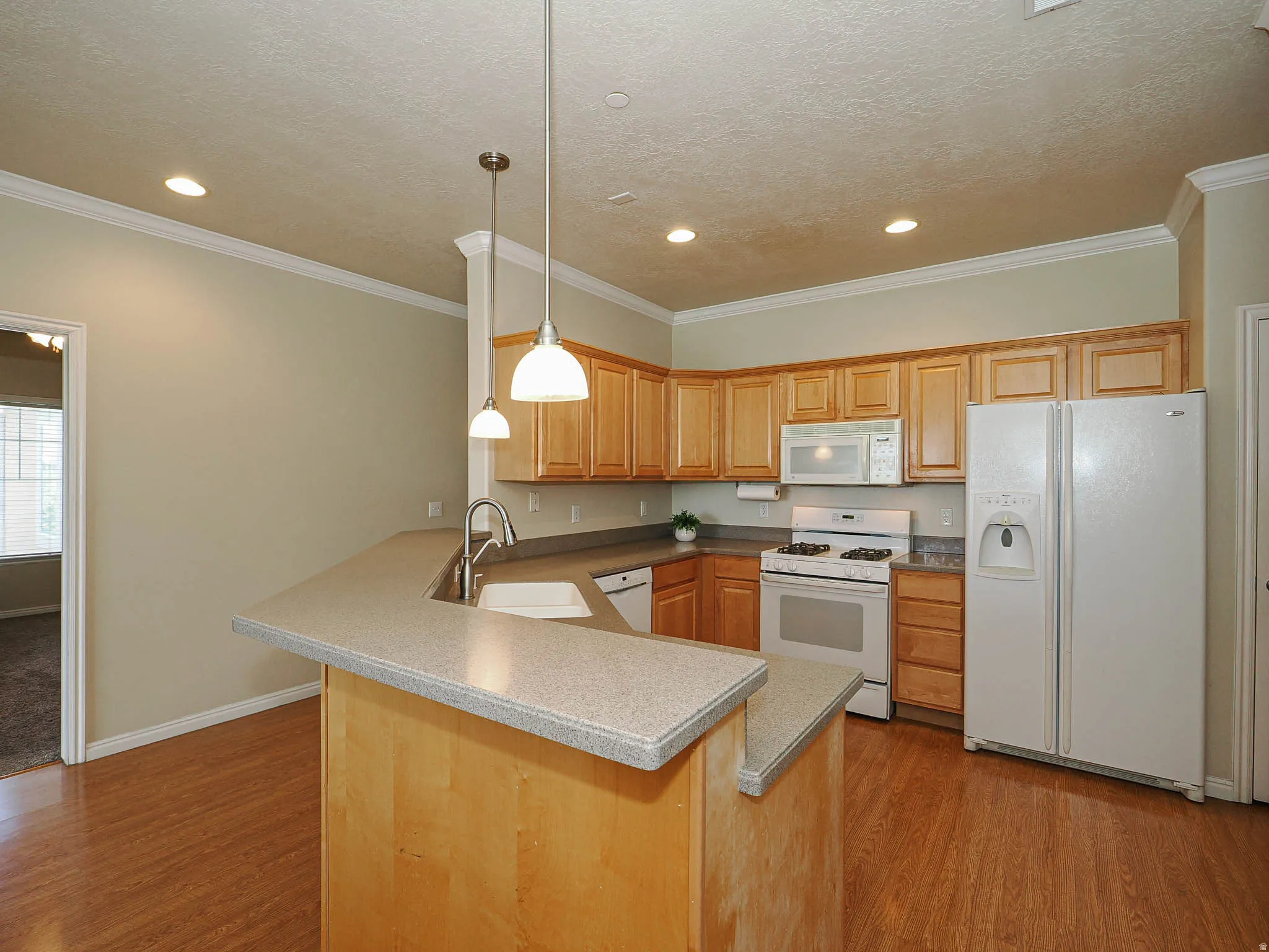 Kitchen featuring wood-finish flooring, light wood cabinetry, white appliances, and a breakfast bar with pendant lighting