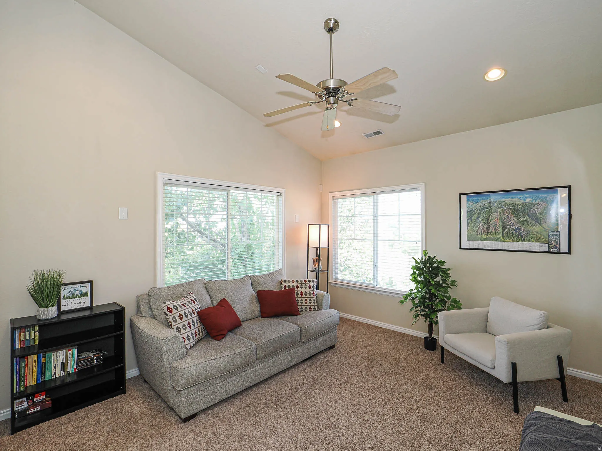 Vaulted ceilings define this space, featuring neutral carpeting and a ceiling fan with integrated lighting