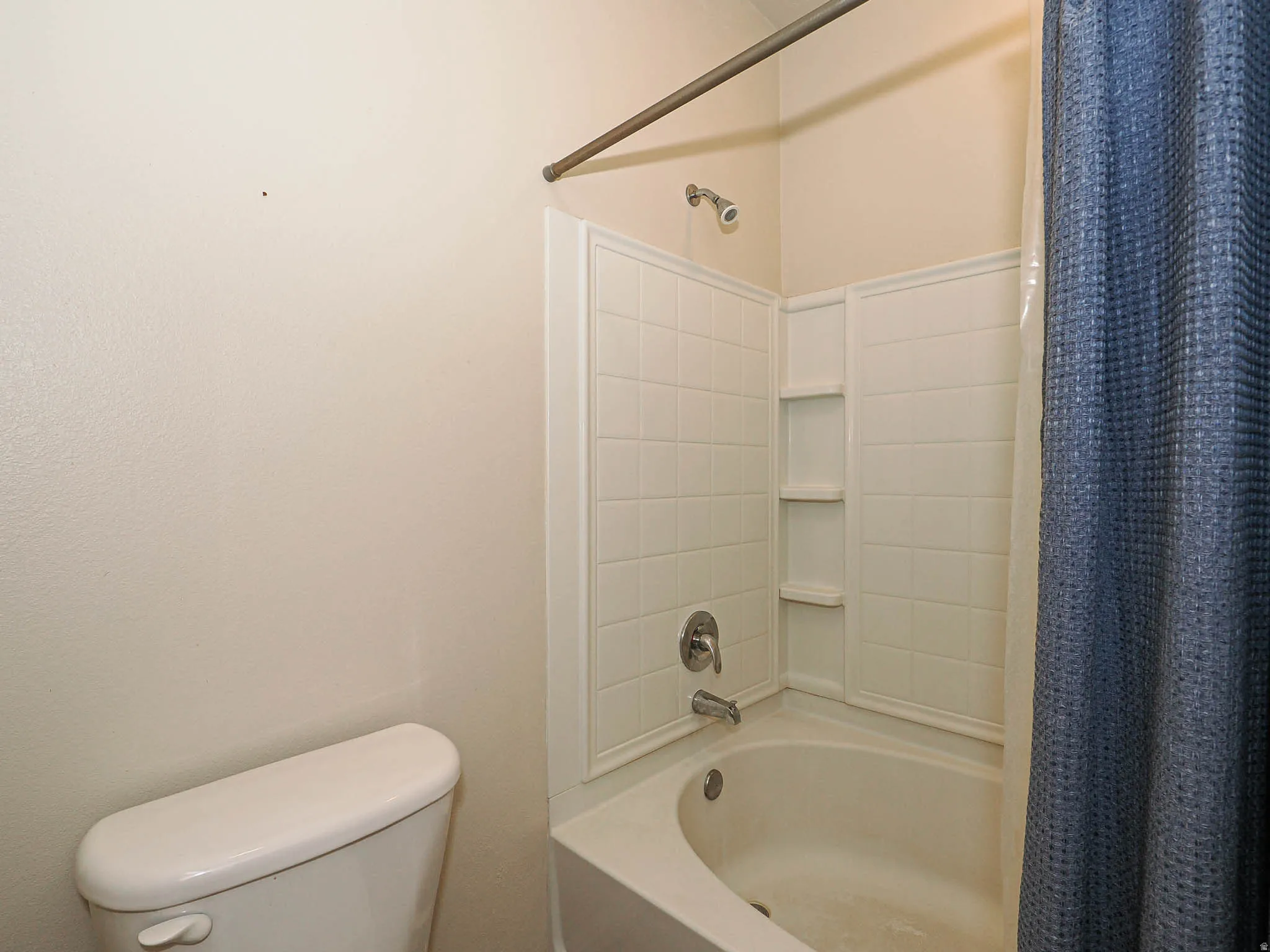 Bathtub and shower combination featuring a curved front, white subway tile surround, and integrated shelving