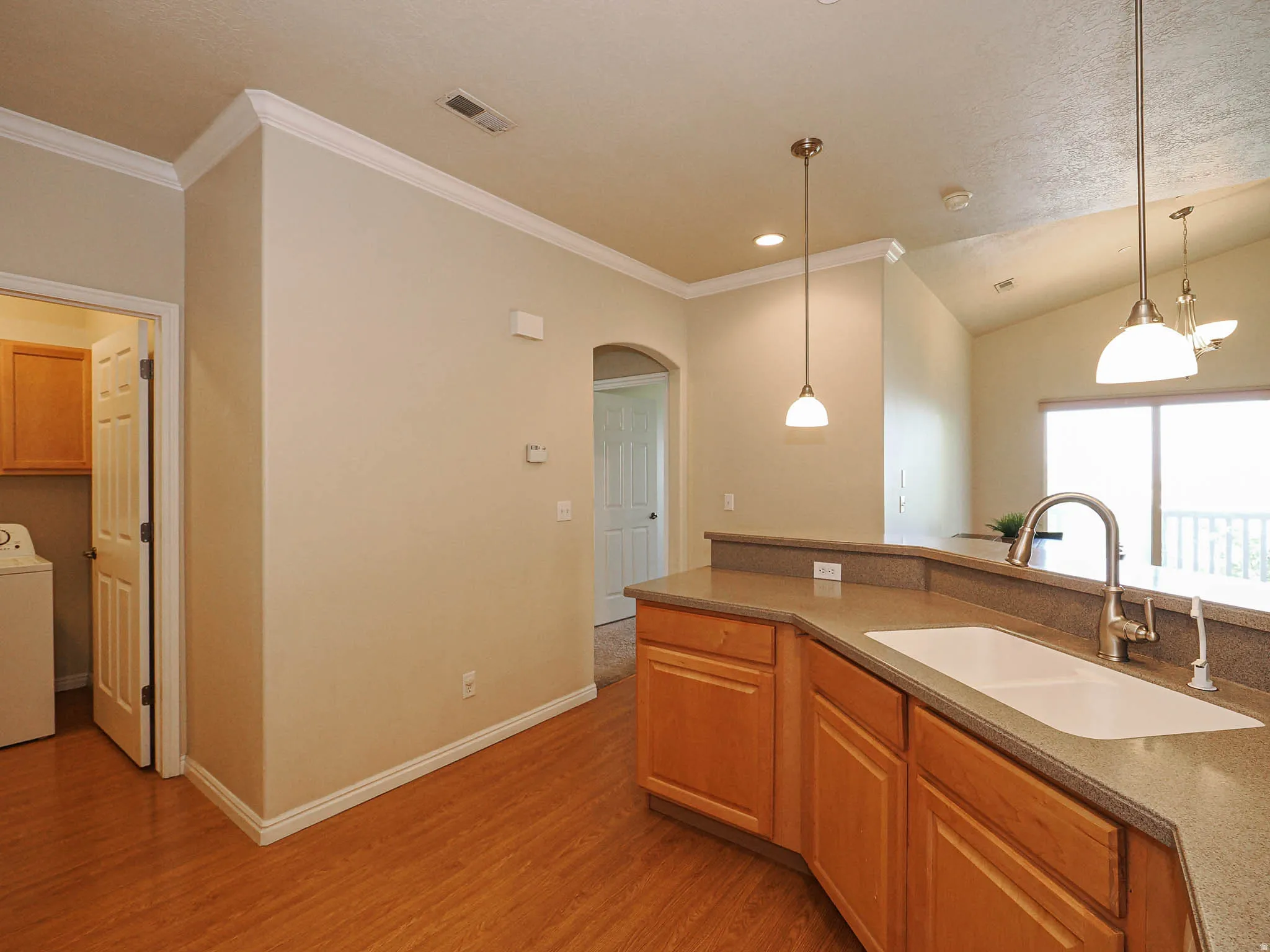 Kitchen featuring wood-finish flooring, light wood cabinetry, a built-in sink with a gooseneck faucet, and pendant lighting