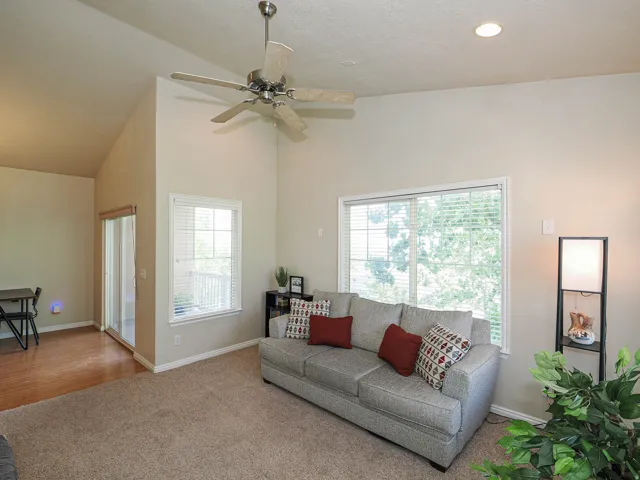 Living area featuring vaulted ceilings, recessed lighting, a ceiling fan, a large window with blinds, and a sliding glass door