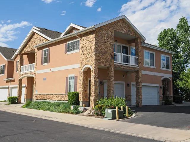 Stucco exterior with stone veneer accents, multiple balconies with white railings, integrated garage doors, and front entry archways