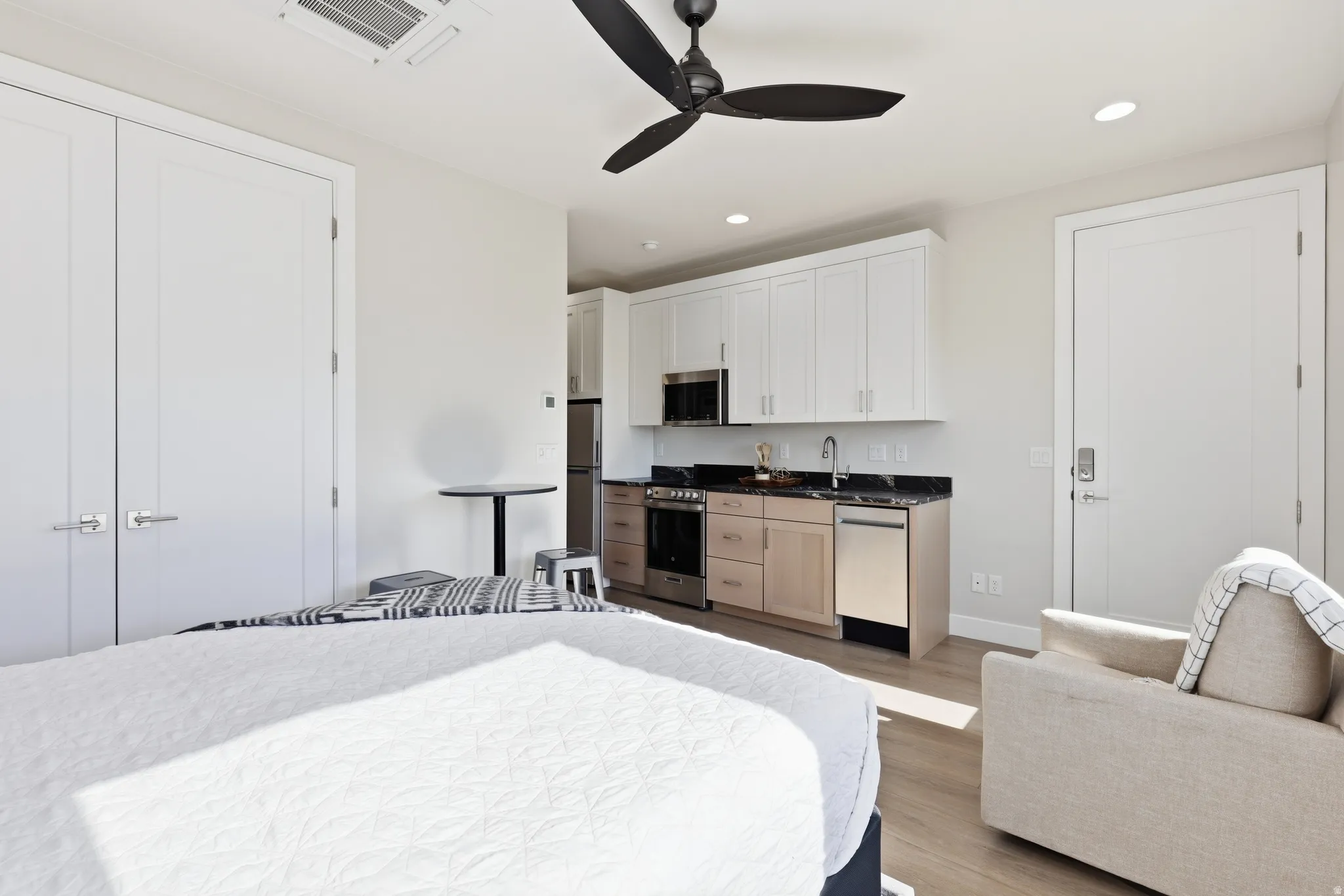 Open-concept living space with a contemporary kitchen featuring stainless steel appliances, dark stone-finish countertops, and white shaker-style cabinetry