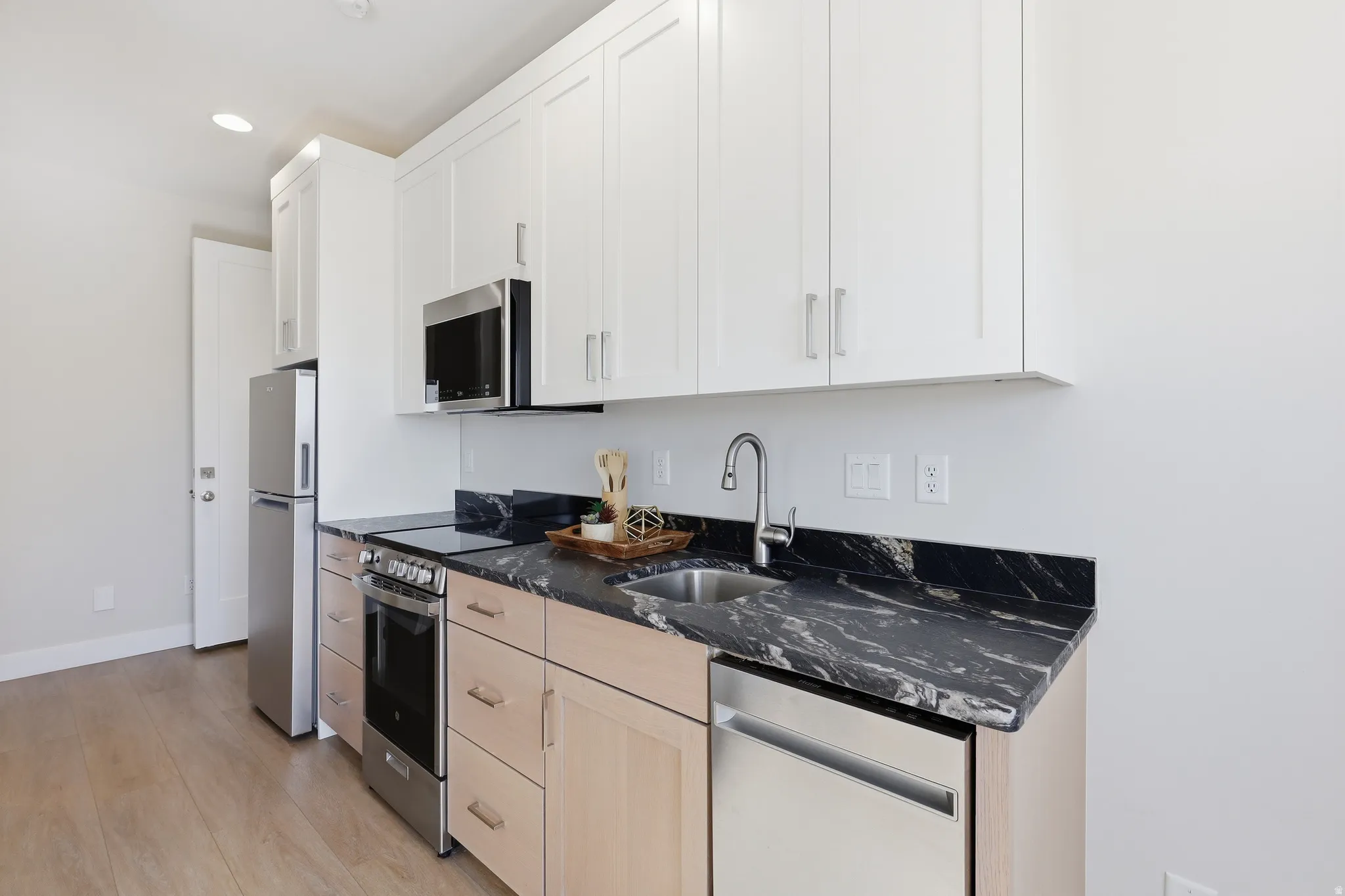 Kitchen featuring white upper cabinetry, wood-finish lower cabinetry, and black patterned countertops