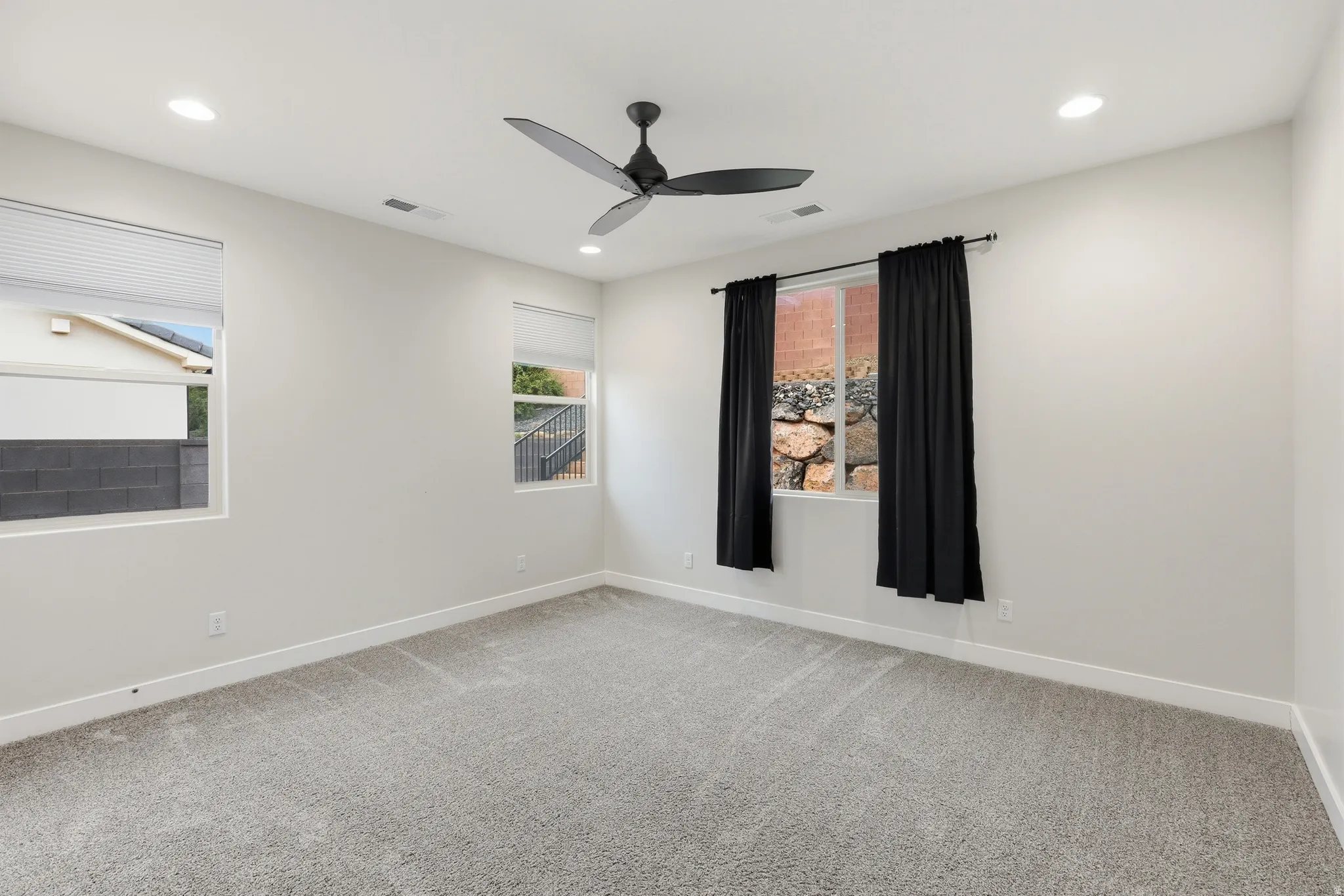 Carpeted room featuring a matte black ceiling fan, recessed lighting, and multiple windows with blinds and curtain rods
