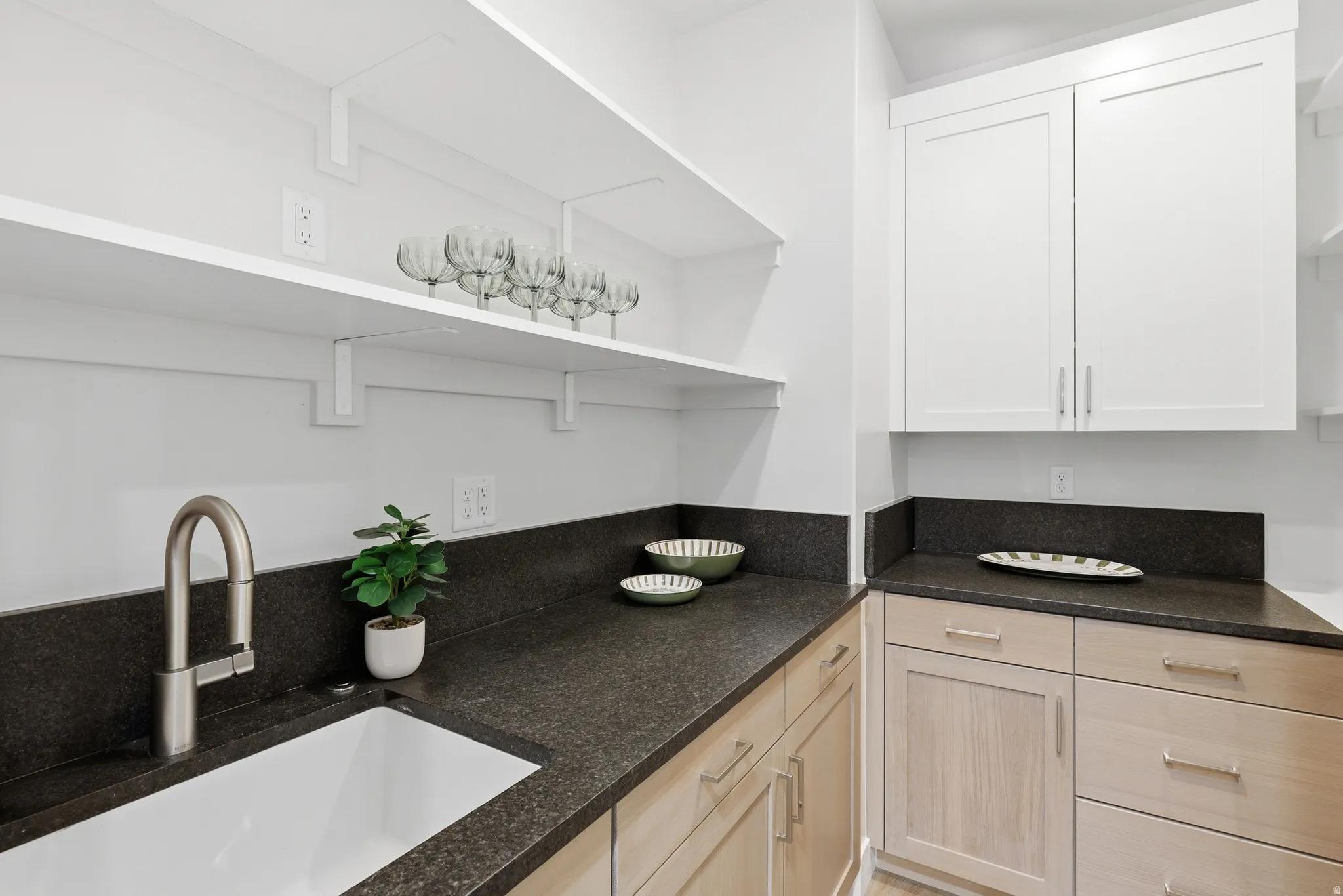 Spacious utility area featuring a deep basin sink with a brushed nickel faucet, dark granite countertops, and light wood-finish lower cabinetry