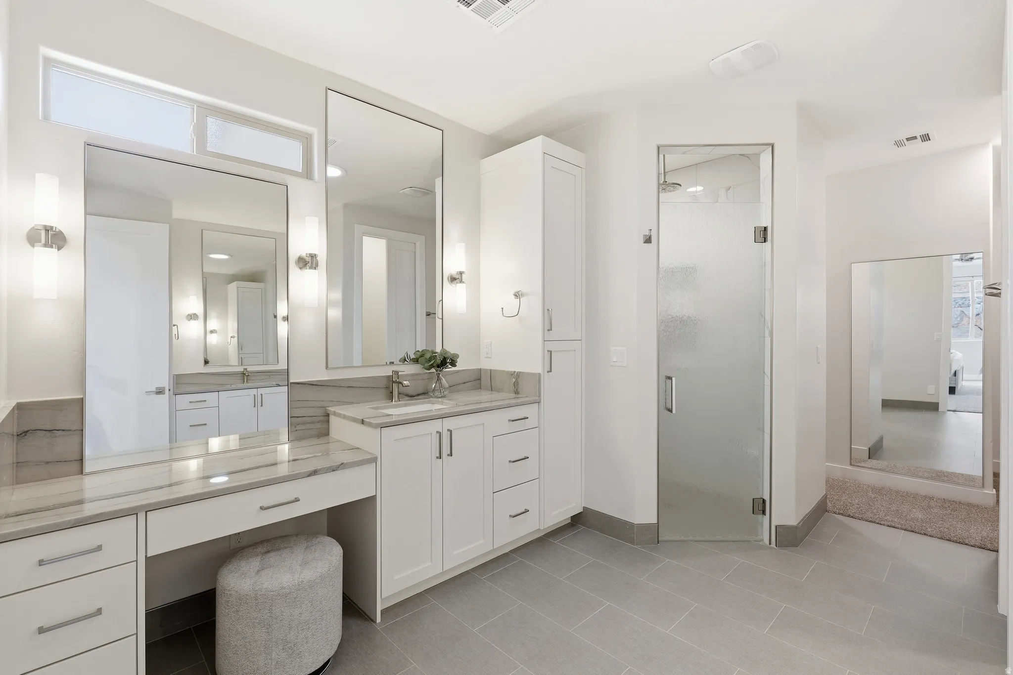 Spacious bathroom featuring a dual vanity, built-in makeup vanity, large rectangular mirrors, and a glass-enclosed shower with a rainfall showerhead