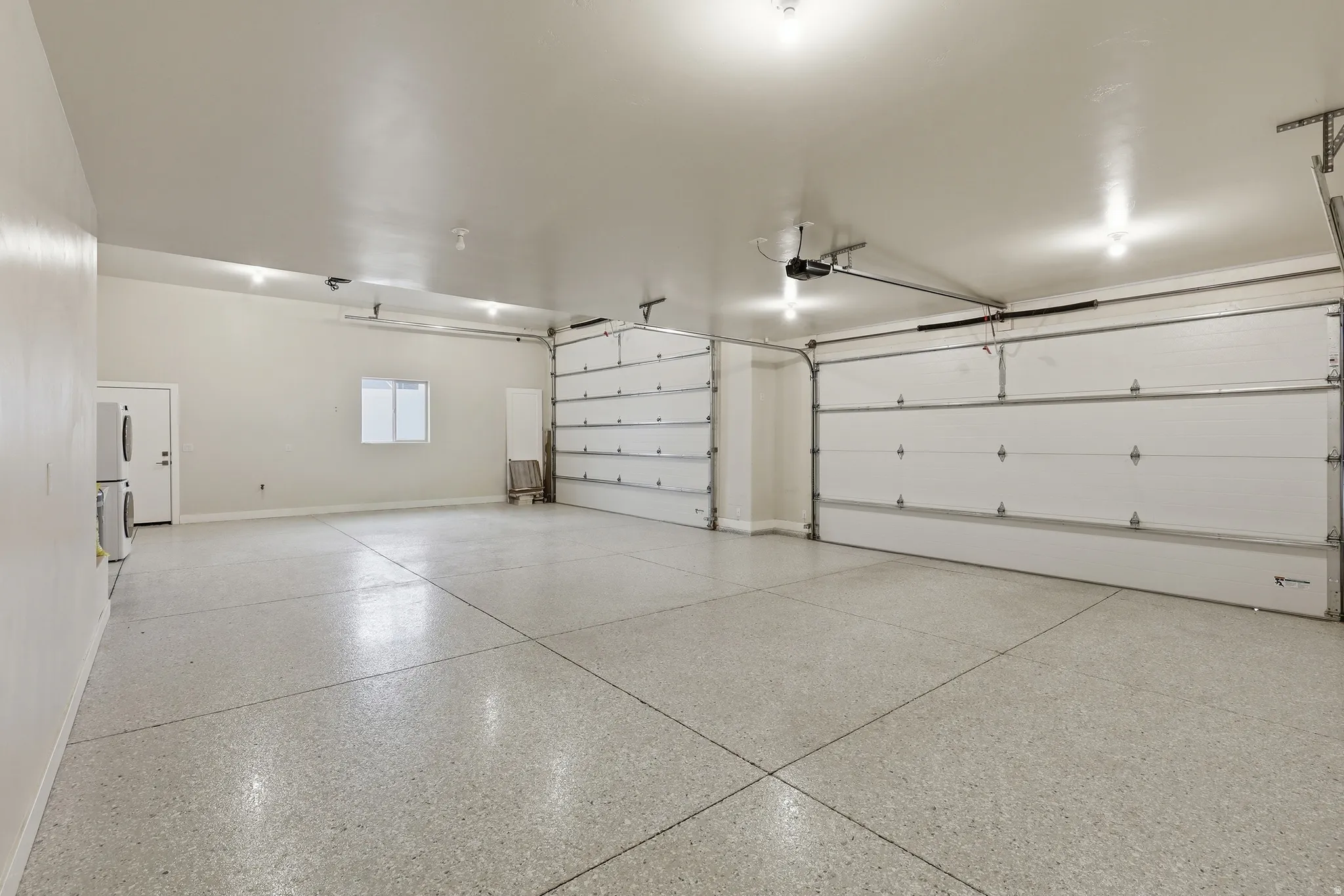 Spacious garage featuring a light-toned epoxy floor, multiple overhead lights, and two large garage doors with automatic openers