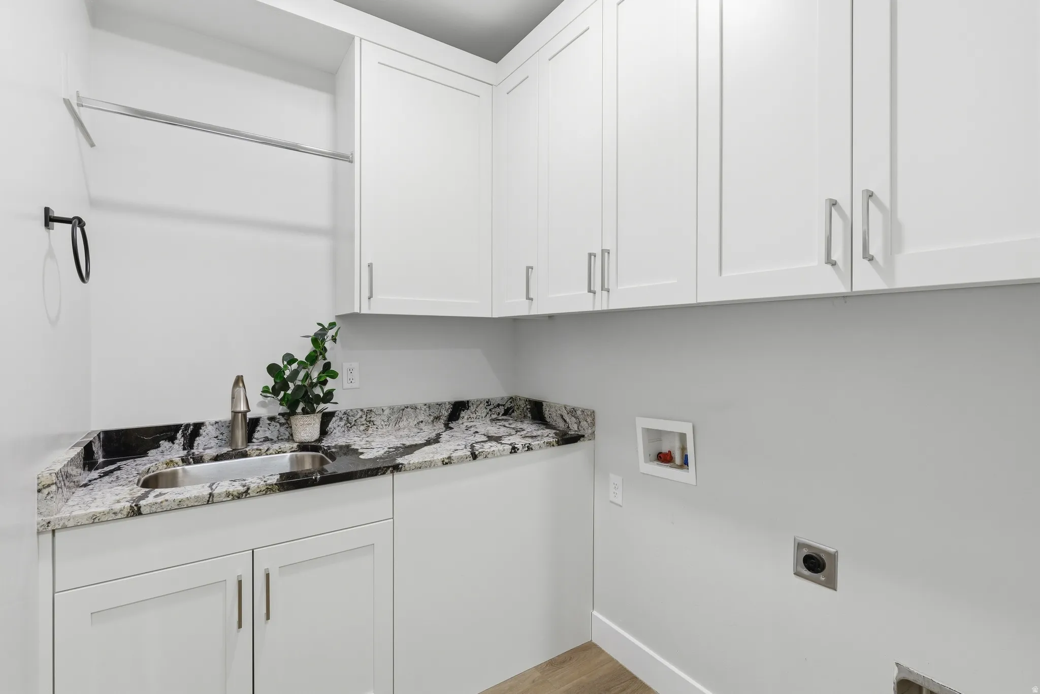 Utility room featuring white shaker cabinetry, patterned stone countertops with an undermount sink, a chrome faucet, and a hanging rod
