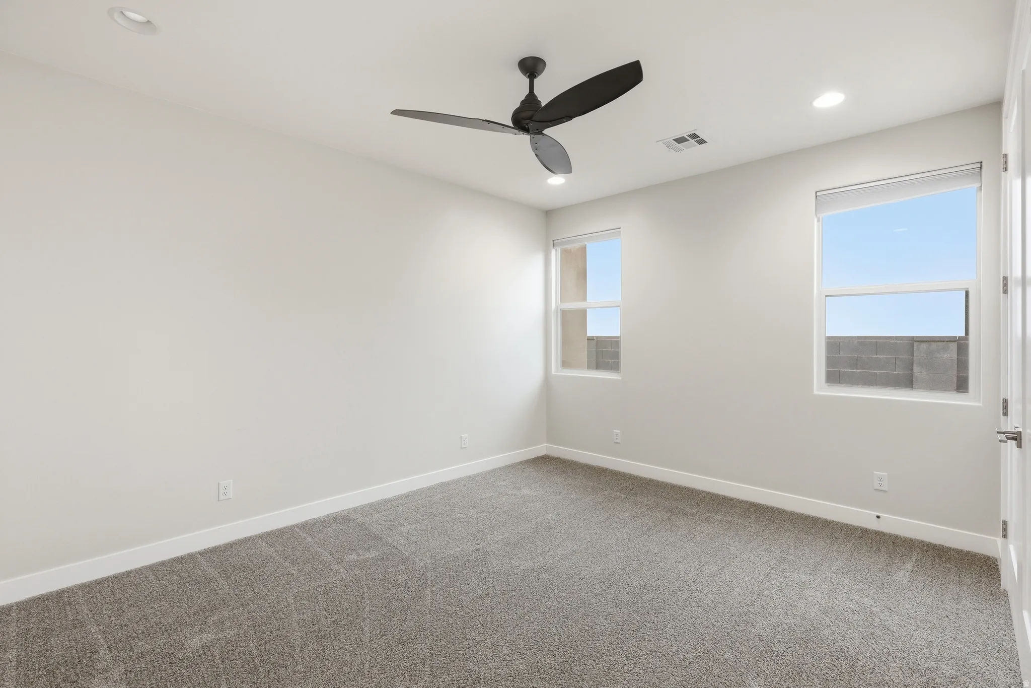 Neutral-toned interior room featuring two windows with roller shades, recessed ceiling lighting, and a dark-toned ceiling fan
